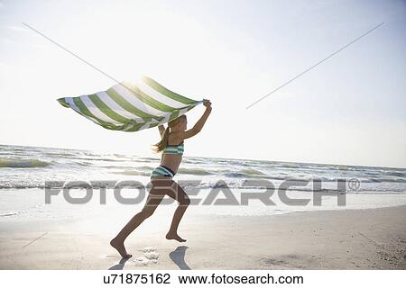 Stock Image - USA, Florida, St. Pete Beach, girl (8-9) running with towel on beach. Fotosearch