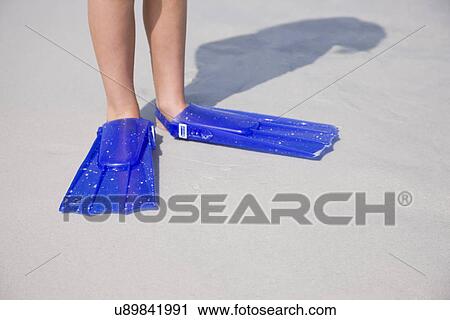 Stock Image - USA, Florida, St. Pete Beach, Girl (8-9) with flippers standing on beach, low section. Fotosearch