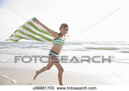 Stock Image - USA, Florida, St. Pete Beach, girl (8-9) running with towel on beach. Fotosearch