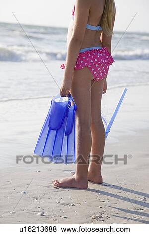 Stock Photo - USA, Florida, St. Pete Beach, girl (8-9) holding flippers on beach. Fotosearch