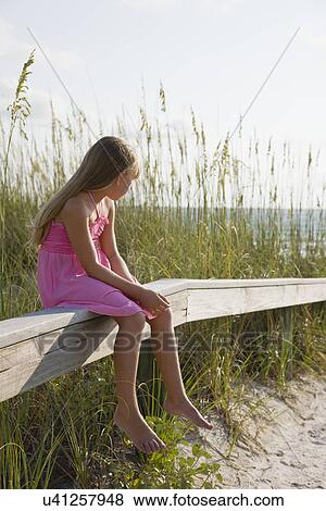 Stock Photo - USA, Florida, St. Pete Beach, Girl (8-9) sitting on wooden rail on beach. Fotosearch