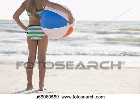 Stock Photo - USA, Florida, St. Pete Beach, girl (8-9) standing with ball on beach. Fotosearch