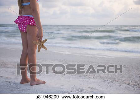Stock Photo - USA, Florida, St. Pete Beach, Girl (8-9) holding starfish and facing ocean, low section. Fotosearch