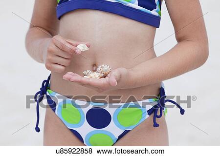 Stock Photo - USA, Florida, St. Pete Beach, Girl (8-9) holding sea shells on beach, mid section. Fotosearch