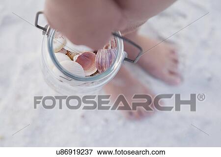 Stock Photo - USA, Florida, St. Pete Beach, Girl (8-9) holding jar of seashells on beach, close-up of hand. Fotosearch