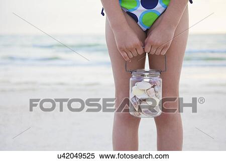 Stock Photography - USA, Florida, St. Pete Beach, Girl (8-9) holding jar of seashells on beach, mid section. Fotosearch