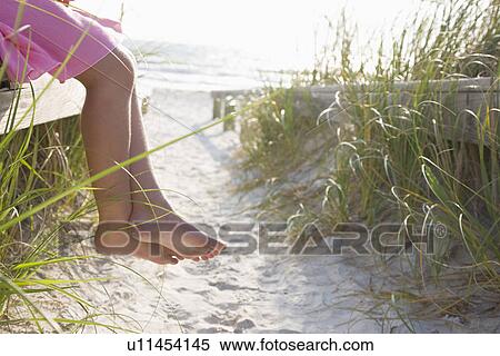 Stock Photography - USA, Florida, St. Pete Beach, Legs of girl (8-9) sitting on rail on beach. Fotosearch