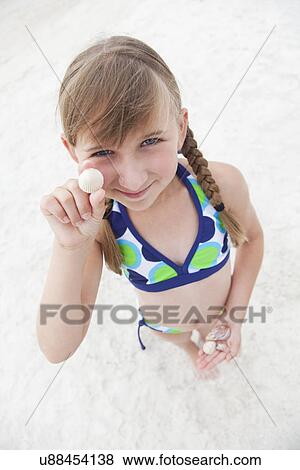 Stock Photo - USA, Florida, St. Pete Beach, Portrait of smiling girl (8-9) holding seashell on beach. Fotosearch