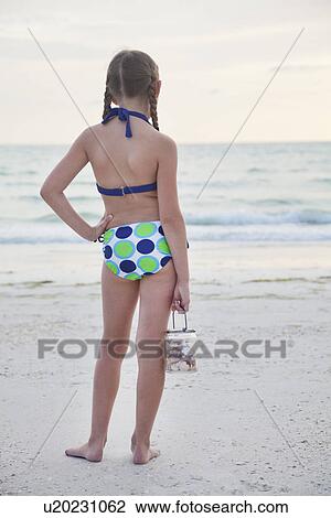 Stock Image - USA, Florida, St. Pete Beach, Rear view of girl (8-9) holding jar of seashells on beach. Fotosearch