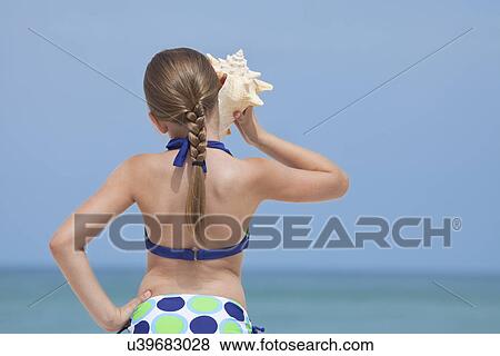 USA, Florida, St. Pete Beach, Rear view of girl (8-9) listening to conch shell on beach View Large Photo Image Stock Photo - USA, Florida, St. Pete Beach, Rear view of girl (8-9) listening to conch shell on beach. Fotosearch