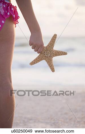 Stock Photo - USA, Florida, St. Pete Beach, Rear view of girl (8-9) holding starfish and facing ocean, mid section. Fotosearch