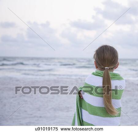 Stock Photography - USA, Florida, St. Pete Beach, Rear view of girl (8-9) wrapped in towel facing ocean. Fotosearch