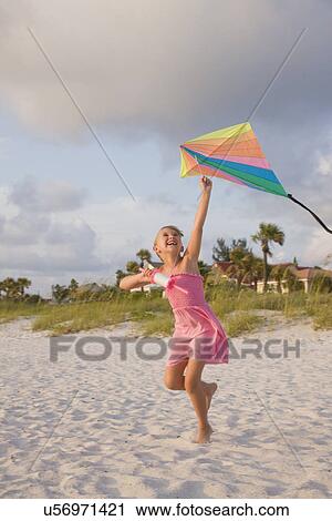 Stock Image - USA, Florida, St. Pete Beach, Smiling girl (8-9) flying kite on beach. Fotosearch