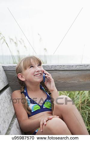 Stock Image - USA, Florida, St. Pete Beach, Smiling girl (8-9) talking on cell phone at beach. Fotosearch
