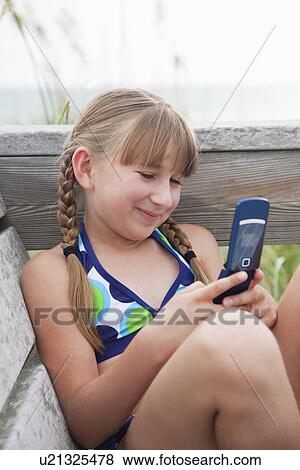 Stock Photo - USA, Florida, St. Pete Beach, Smiling girl (8-9) texting on cell phone at beach. Fotosearch