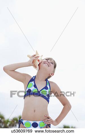USA, Florida, St. Pete Beach, Smiling girl (8-9) listening to conch shell on beach View Large Photo Image Stock Photo - USA, Florida, St. Pete Beach, Smiling girl (8-9) listening to conch shell on beach. Fotosearch