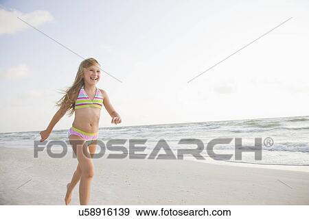Stock Photo - USA, Florida, St. Pete Beach, Smiling girl (8-9) in bikini walking on beach. Fotosearch