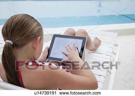 Stock Image - USA, Florida, St. Petersburg, Girl (10-11) sitting on poolside, using digital tablet. Fotosearch