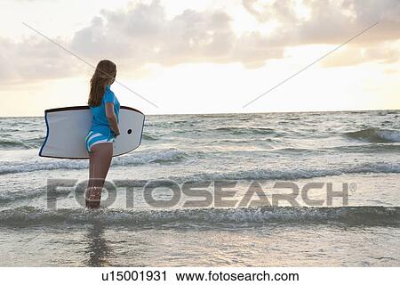 Stock Image - USA, Florida, St. Petersburg, girl (12-13) holding boogie board and looking at view. Fotosearch