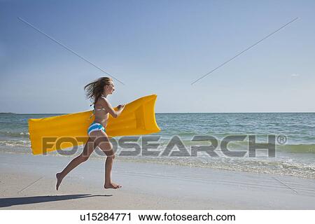 Stock Image - USA, Florida, St. Petersburg, girl (12-13) holding pool raft running along beach. Fotosearch