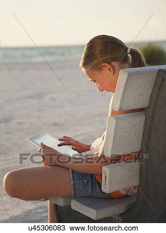 Stock Image - USA, Florida, St. Petersburg, Girl (10-11) using digital tablet on beach at sunset. Fotosearch
