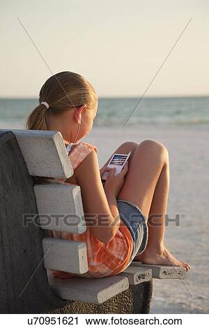 Stock Image - USA, Florida, St. Petersburg, Girl (10-11) using mp3 player on beach at sunset. Fotosearch
