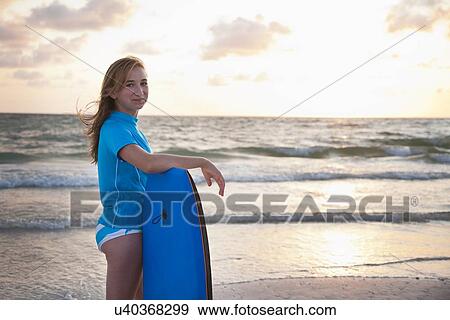Stock Photo - USA, Florida, St. Petersburg, girl (12-13) with boogie board looking at horizon over water. Fotosearch