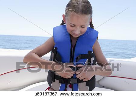 Stock Photo - USA, Florida, St. Petersburg, Girl (10-11) fastening life jacket in speedboat. Fotosearch