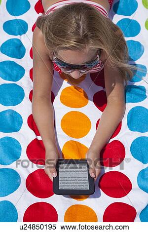 Stock Photography - USA, Florida, St. Petersburg, girl (12-13) laying down on beach towel and holding digital tablet. Fotosearch