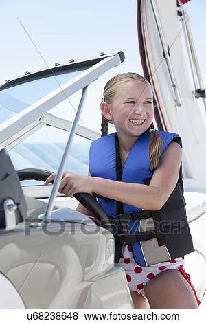 Stock Photo - USA, Florida, St. Petersburg, Smilling girl (10-11) wearing life jacket steering speedboat. Fotosearch