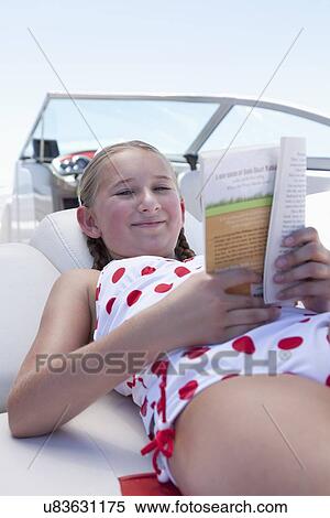 Stock Photography - USA, Florida, St. Petersburg, Smilling girl (10-11) reading book on yacht. Fotosearch