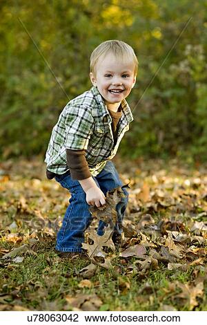 Stock Image - USA, Illinois, Brimfield Boy (2-3) playing with Autumn leaves in park. Fotosearch