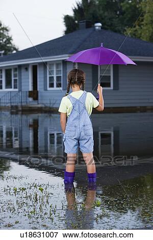 Stock Photo - USA, Illinois, Chillicothe, Mixed race girl (8-9) standing in water and holding umbrella, rear view. Fotosearch
