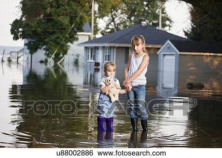 Stock Photograph - USA, Illinois, Chillicothe, Two girls (2-3, 8-9) holding hands, Standing in water and looking at camera. Fotosearch