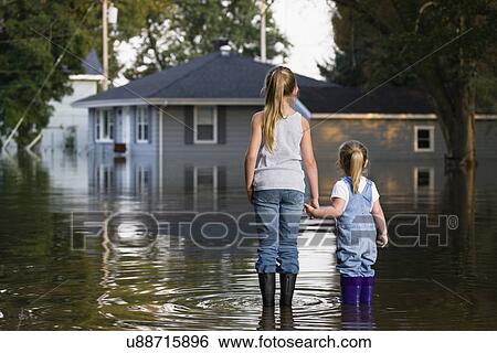 Stock Photograph - USA, Illinois, Chillicothe, Two girls (2-3, 8-9) holding hands and standing in water, rear view. Fotosearch