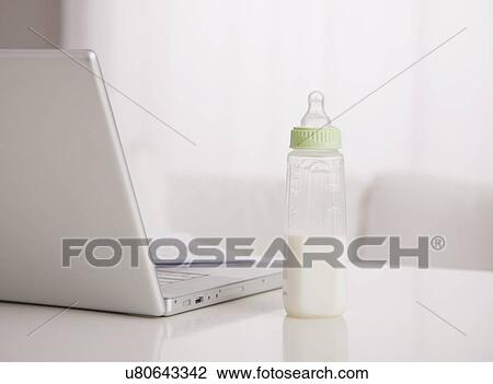 Stock Image - USA, Illinois, Metamora, baby bottle with milk and laptop on table. Fotosearch
