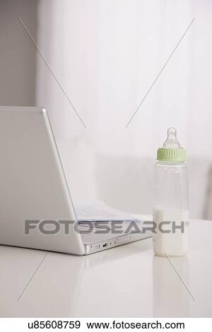 Stock Photo - USA, Illinois, Metamora, baby bottle with milk and laptop on table. Fotosearch