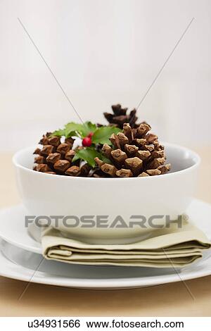 Stock Photograph - USA, Illinois, Metamora, Bowl with pine cones and holly on table. Fotosearch