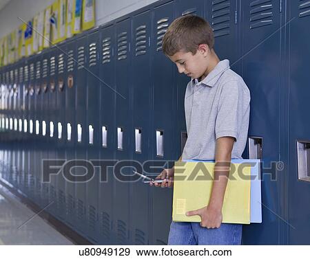 Stock Photo - USA, Illinois, Metamora, Boy (10-11) standing at lockers in school corridor and text messaging. Fotosearch