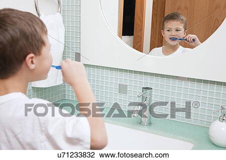Stock Image - USA, Illinois, Metamora, Boy (6-7) brushing teeth in bathroom. Fotosearch