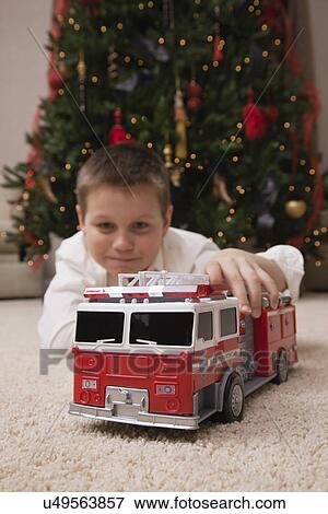 USA, Illinois, Metamora, boy (8-9) lying in front of Christmas tree playing with new toy car View Large Photo Image Stock Photo - USA, Illinois, Metamora, boy (8-9) lying in front of Christmas tree playing with new toy car. Fotosearch