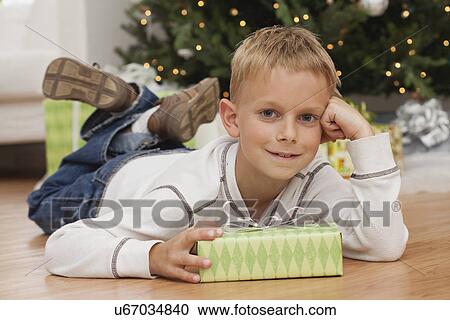 Stock Image - USA, Illinois, Metamora, Boy (8-9) with gift box lying on floor. Fotosearch