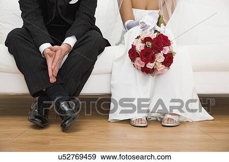 Stock Photo - USA, Illinois, Metamora, Bride and groom sitting on sofa. Fotosearch