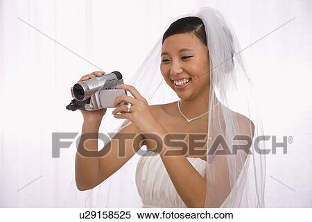 Stock Photography - USA, Illinois, Metamora, Bride using camcorder. Fotosearch