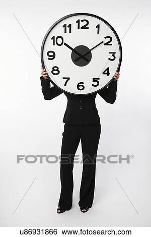 Stock Photograph - USA, Illinois, Metamora, Business woman holding large clock over head. Fotosearch