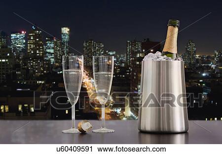 Stock Image - USA, Illinois, Metamora, Champagne flutes and bottle in ice bucket with downtown skyline in background. Fotosearch