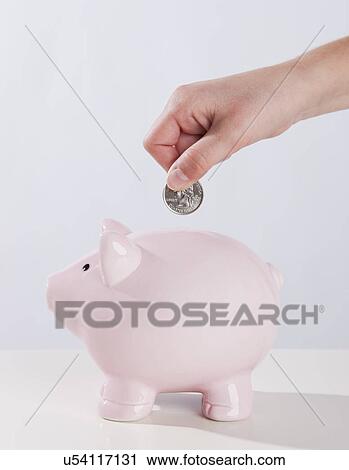 Stock Image - USA, Illinois, Metamora, Child's (10-11) hand putting money into piggy bank. Fotosearch