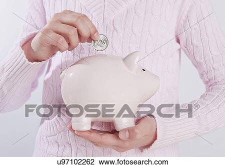 Stock Image - USA, Illinois, Metamora, Child's (10-11) hand putting money into piggy bank. Fotosearch
