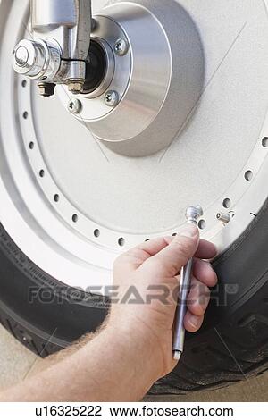 Stock Image - USA, Illinois, Metamora, Close up of man's hand checking pressure in motorcycle tire. Fotosearch