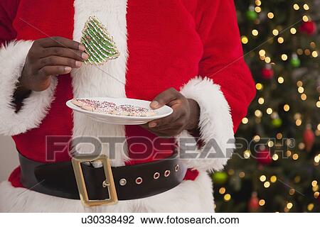 Stock Image - USA, Illinois, Metamora, Close up of hands of Santa Claus holding cookie. Fotosearch